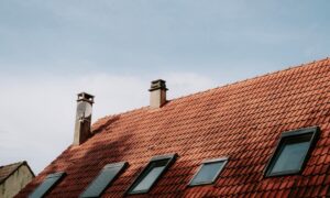A red-tiled roof with three skylights and two chimneys against a clear blue sky.