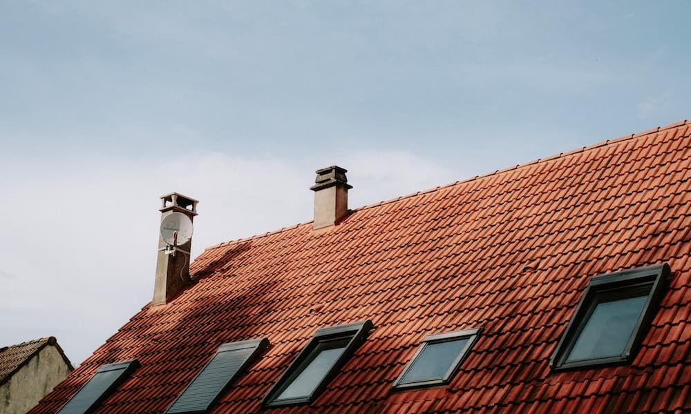 A red-tiled roof with three skylights and two chimneys against a clear blue sky.
