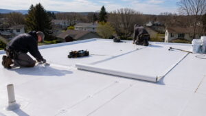 Two roofing contractors installing white PVC membrane on a flat residential roof.