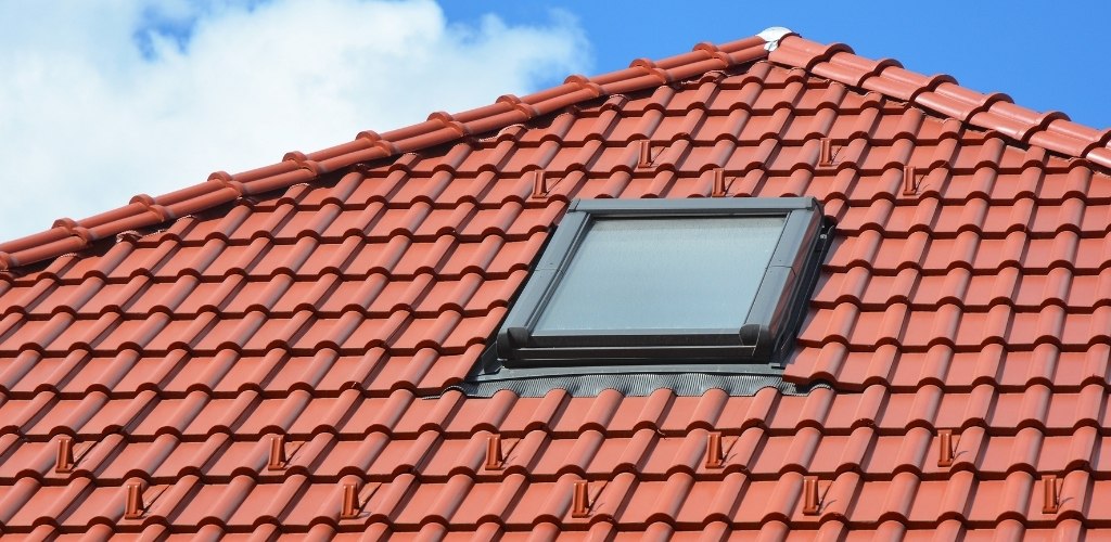 pitched roof covered in interlocking red ceramic or clay tiles featuring a central skylight
